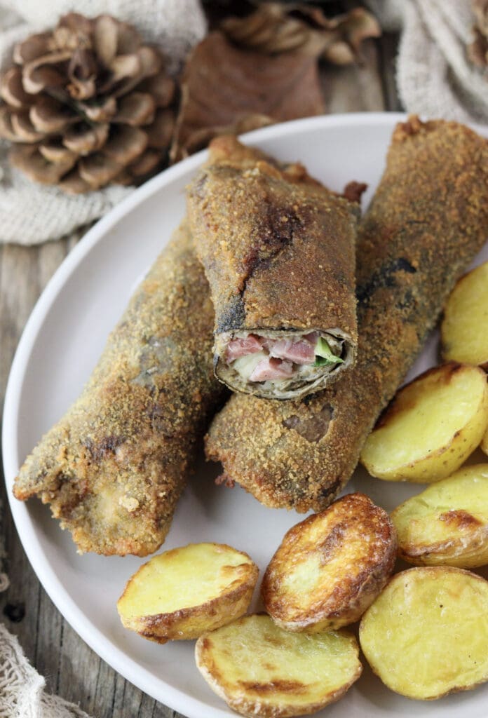 A plate with breaded, fried parasol mushroom rolls with mozarella and bacon poping out of a sliced roll on top.